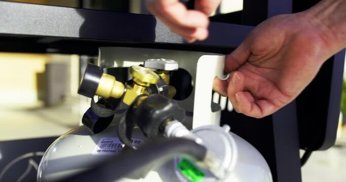 Adult hands turning valve on propane tank beneath grill - closeup