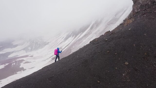 Lonely female backpacker dressed rain cover with backpack and trekking poles making acclimatization trek around Lenin peak base camp climbing Petrovsky Peak 4910 m, Pamir mountains range, Kyrgyzstan.