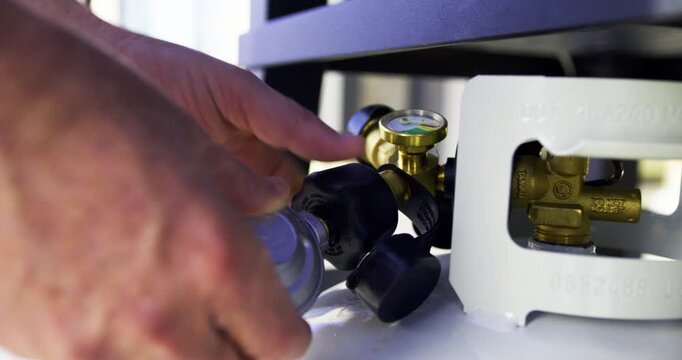 Hands attaching gas hose to propane tank - closeup