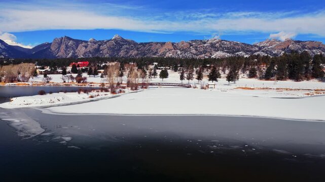 Lake Estes frozen ice lakeside Mummy Range Estes Park aerial drone Colorado Front Range Rocky Mountains National Park Larimer County landscape winter sunny blue sky morning Olympus Dam circle right