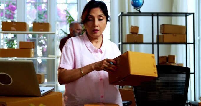 Indian senior couple doing E-commerce business from home, busy working in office managing online orders, packing parcels, dispatching boxes, taking customer calls and handling inventory together