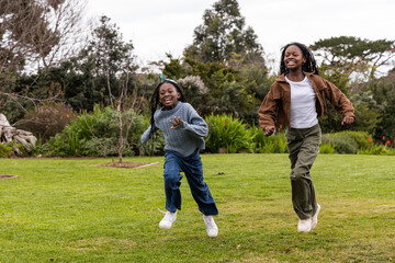 African American girls aged 8-12 running across lawn in park, wearing teal headband and sneakers