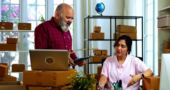 Indian senior couple showing stress doing E-commerce business from home while managing online orders, dispatching parcels, packing cardboard boxes and handling hectic workload in home office