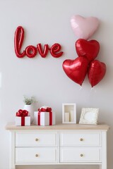 the word love written in red foil balloons on a light colored wall, decorated with heartshaped balloon bouquets and small gift boxes placed next to a white chest of drawers.