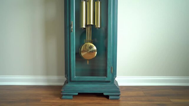 A tall teal-painted clock with a pendulum and weights is captured against a light-colored wall and wooden flooring. The clock is antique-looking