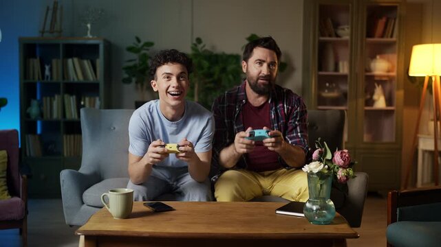 Happy teenage boy and his father playing video game using joysticks, having fun