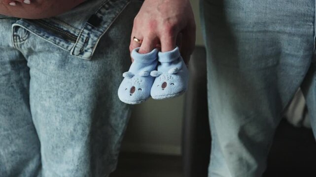 Pregnant woman belly and man holding blue baby booties. Expectant parents waiting for their son in a tender moment. Ideal for maternity blogs, family planning, and pregnancy announcements.