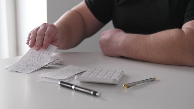 Person At Desk Sorting Invoices, Closeup On Forearms And Pens, Stack Of Bills And Receipts, Folded Arms Signaling Pause, Quiet Office Lighting, Bookkeeper Reviewing Payments And Budget