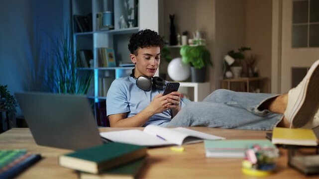 Lazy teenage boy playing game on phone instead of studying, procrastination