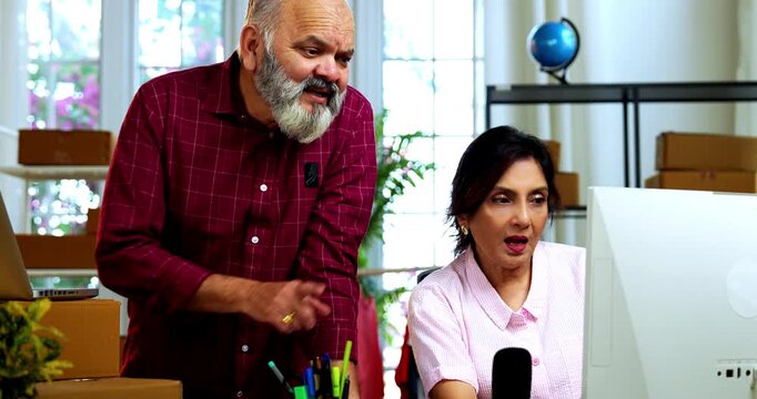 Indian senior couple celebrating success in home based E-commerce business while managing online orders, dispatching parcels, packing cardboard boxes and working together in home office