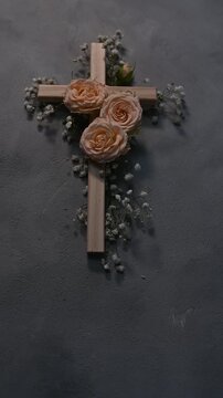 Wooden christian cross vectical with pink roses and gypsophila flowers on a dark wall representing faith and symbolizing resurrection easter faith