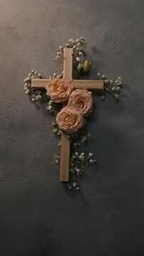 Wooden christian cross vectical with pink roses and gypsophila flowers on a dark wall representing faith and resurrection symbolizing faith, easter