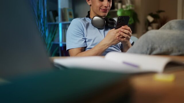 Happy adolescent boy texting on cellphone, procrastinating instead of studying