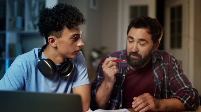 Caring father helping teen son with homework, explaining task, family support