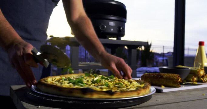 Low, medium shot of veggie pizza and cook cutting it with roller