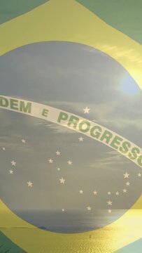 Vertical video: Camera panning upward pushing Brazil flag overlay showing coastline as sun shifting