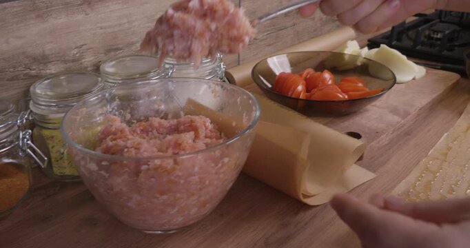 A woman's hands, using a spoon, spoon freshly chopped meat onto oiled parchment paper on a wooden countertop. The woman prepares a home-cooked meal from ingredients found nearby in the kitchen.
