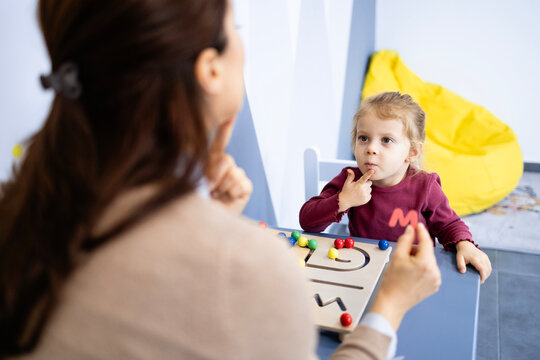 Speech pathologist guiding a young girl through mouth movements and interactive exercises to improve articulation, communication, and early language development in a clinic