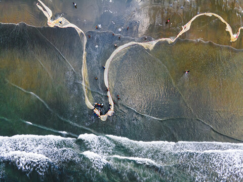 Cox's Bazar, Bangladesh - 16 May 2024: Aerial view of fishing nets cast into the turquoise sea where fishermen work along the sandy beach, creating a mesmerizing blend of textures and colors.