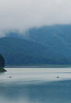 Cherrapunji, India - 28 July 2023: View of tranquil waters reflecting the soft, misty mountains, two small boats gliding across the serene expanse.