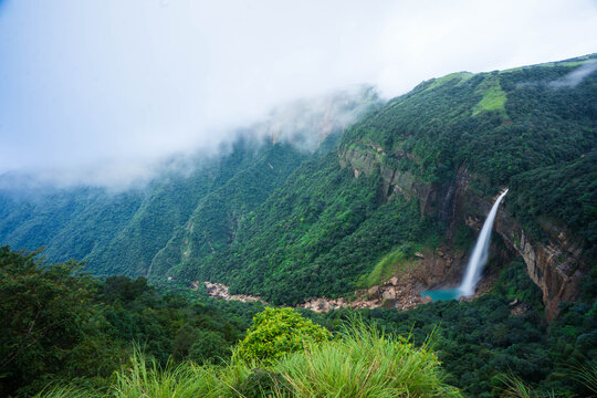 Cherrapunji, India - 27 July 2023: View of the majestic Nohkalikai Falls plunging from lush green cliffs into a turquoise pool, shrouded in mystic clouds, creating a breathtaking vista.