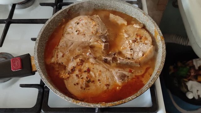 Three pieces of pork is simmering in red sauce in frying pan