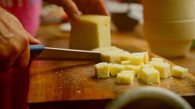 Close-up of an artisan's hands slicing traditional handmade cheese (cașcaval) on a rustic wooden board at a local folk festival.