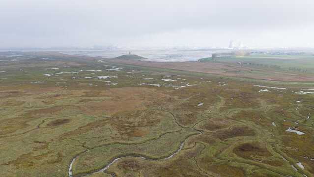Aerial view of the landscape where a small building is visible on a small hill, under a cloudy sky, Nieuw Namen, Zeeland, Netherlands.