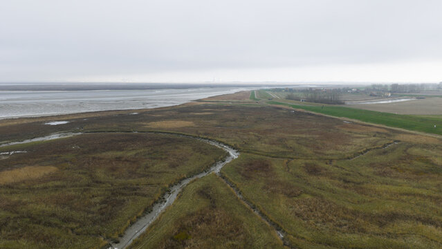 Aerial view of winding waterways carving through the marshland, where muted earth tones meet the somber horizon, Nieuw Namen, Zeeland, Netherlands.