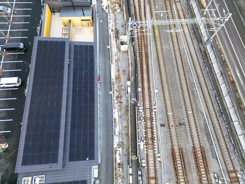 Aerial view of train tracks running parallel to a building with solar panels, contrasting the industrial and sustainable, Karuizawa, Nagano, Japan.