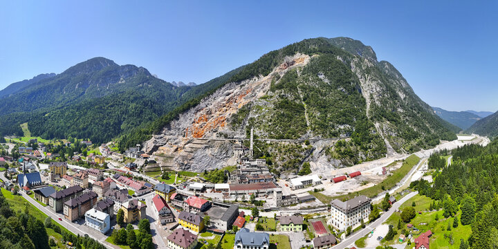 Aerial view of the town nestled among the verdant forests and rugged, rocky mountains, with a stark contrast between the greenery and the exposed earth, Cave del Predil, Friuli-Venezia Giulia, Italy.