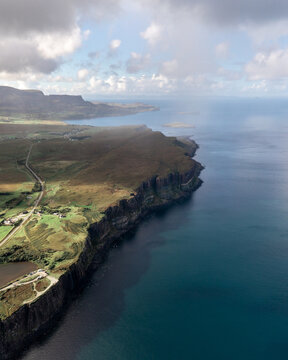 Aerial view of rugged cliffs meet the turquoise sea under a sky dappled with soft clouds, defining the dramatic coastline of Portree, Scotland, United Kingdom.