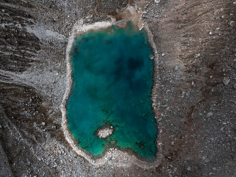 Aerial view of a turquoise lake surrounded by rocky terrain, its waters reflecting the sky above, creating a serene contrast with the rugged landscape, Huaraz, Ancash, Peru.