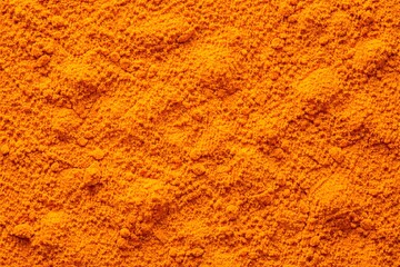 Ground Turmeric Powder Flat Lay Texture Background. Macro flat lay of ground turmeric powder in deep earthy golden yellow and amber tones, fine powder surface with subtle mounds.