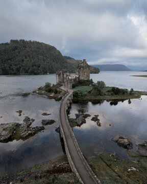 Aerial view of Eilean Donan Castle and bridge reflected in the still loch waters under a cloudy sky, Kyle of Lochalsh, Scotland, United Kingdom.