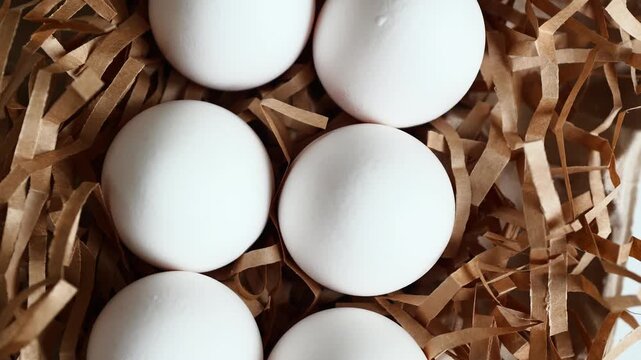 Fresh white eggs are placed in a nest made of brown paper strips on a neutral background