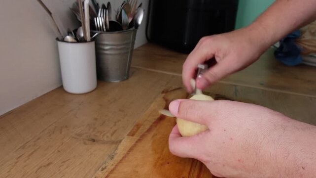 Male hands peel new potatoes with peeler on wooden kitchen counter top
