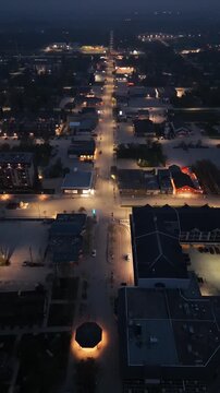 Vertical drone aerial moving backward over Main Street in Gimli Manitoba at night. Small town roadway with streetlights, vehicles and illuminated buildings under dark sky.