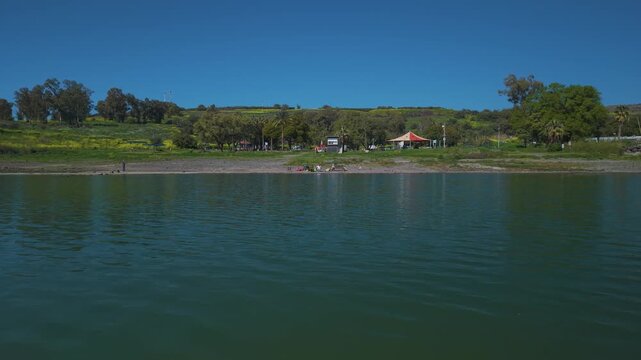 Lake Kinneret in Israel showing fishermen with rods sitting in the shallow water at the rocky Amnon Beach coast