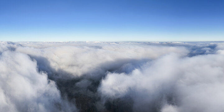 Aerial view of a sea of clouds gently blankets the landscape below, contrasting with the clear blue sky above, Windpark Freilanderalm, Styria, Austria.