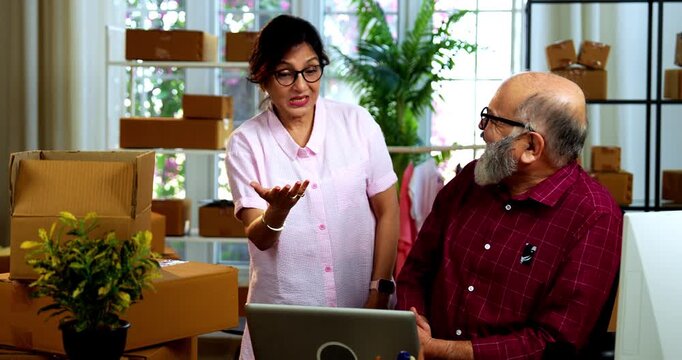 Indian senior couple celebrating success in home based E-commerce business while managing online orders, dispatching parcels, packing cardboard boxes and working together in home office