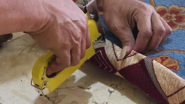 Close-up of craftsman hands upholstering furniture seat with fabric and staple gun