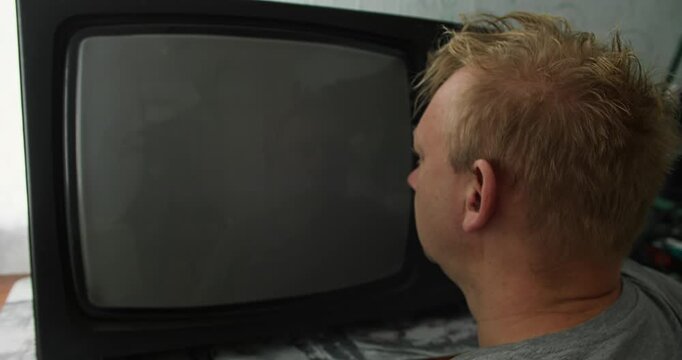 Man stares at CRT television with analog TV static as the screen turns off and becomes dark, while he continues watching. Media hypnosis, mindless viewing, and residual screen influence