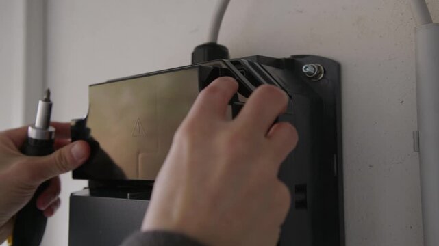 Close-up of an EV charging station being closed. The internal electronics, DIP switches, wiring terminals, and flashing status LEDs are visible during configuration or repair.