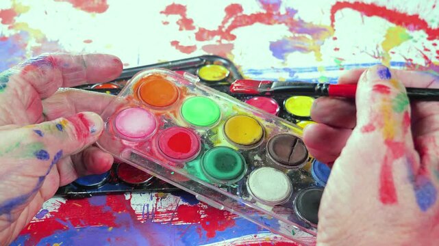 The hands of the artist, work to create creative images in art. Art paints and brushes, applying multi-coloured strokes to the canvas using palette, gouache and watercolour.