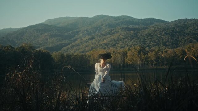 Graceful Woman Dressed In White With Suitcase Taking Slow Walk Near Tranquil Mountain Shoreline