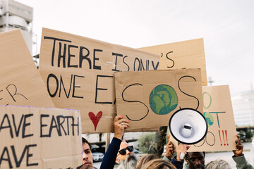 Group of activists raising cardboard placards during an environmental demonstration, advocating for global warming awareness, holding a megaphone and showing planet earth illustrations © Xavier Lorenzo