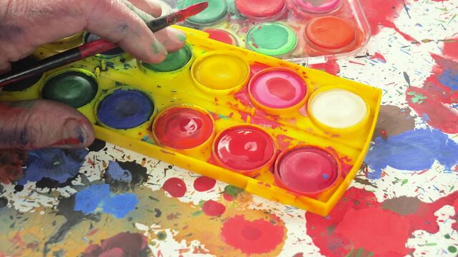 The hands of the artist, work to create creative images in art. Art paints and brushes, applying multi-coloured strokes to the canvas using palette, gouache and watercolour.