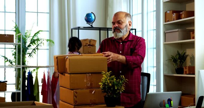 Indian senior couple making products ready to be dispatched, while doing E-commerce business from home managing online orders, packing cardboard boxes, counting garments and preparing parcels