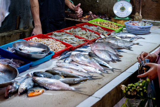 Fresh raw sea fish, shrimp and mussels displayed on white table with vendor and customer at local traditional wet market